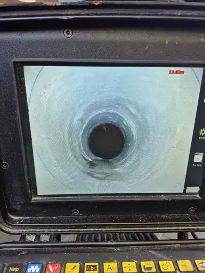 no-dig drain repair — CCTV monitor view down a 100mm underground drain pipe at 13.83 metres showing a smooth, glossy cured 100mm patch liner sealing a previously cracked clay section with the displaced joint covered.