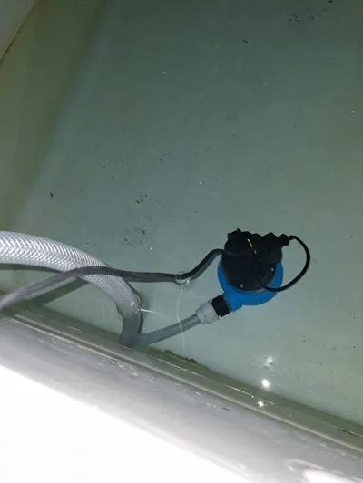 water hygiene service — clear flexible drain-down hose feeding into a low-voltage submersible pump fitted inside a GRP cold water storage tank during a Legionella ACOP L8 tank clean.