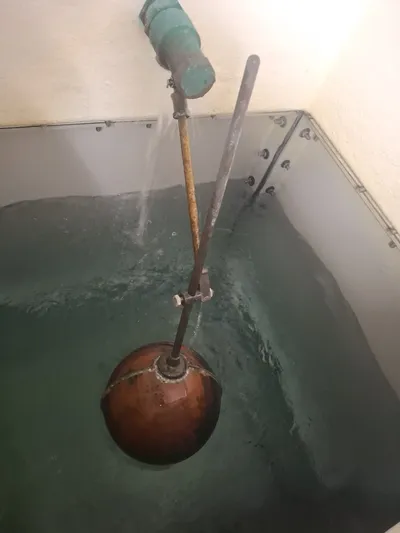 repair — large copper float ball on a brass ball valve arm inside a sectional GRP cold water storage tank, with water flowing from the inlet during a level adjustment and reseating service.