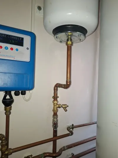install — copper sealed-system pipework feeding a wall-mounted white expansion vessel with new brass drain-off valve, beside a blue Mikrofill 3 pressurisation unit displaying 1.9 bar correct system pressure.