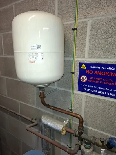 G3 service — wall-mounted Varem 12-litre potable expansion vessel above neatly soldered copper pipework, beside a yellow gas installation No Smoking safety sign in a UK domestic plant area.